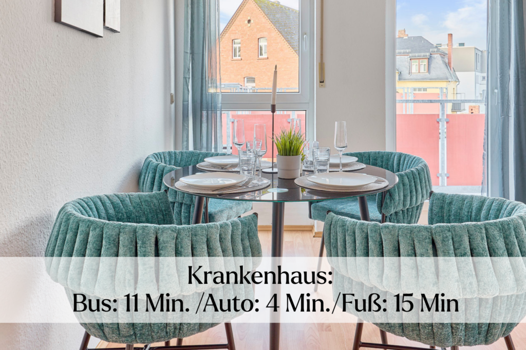 Essbereich mit rundem Tisch und grünen Stühlen am Fenster und Hinweis auf Krankenhaus in der Nähe